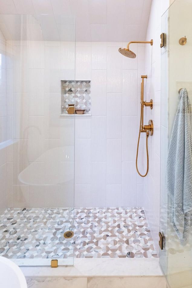 Primary bathroom close-up of the glass door shower with marble mosaic floors and niche.